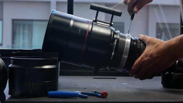 Using a screwdriver to remove screws on the barrel of a big movie camera zoom lens