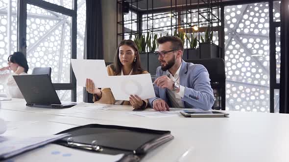 Modern Business Man and Woman Comparing Different Reports with Diagrammas in the Office Room