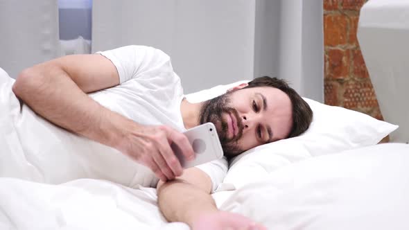 Man on Smartphone Browsing Email and Messages Lying in Bed on Side