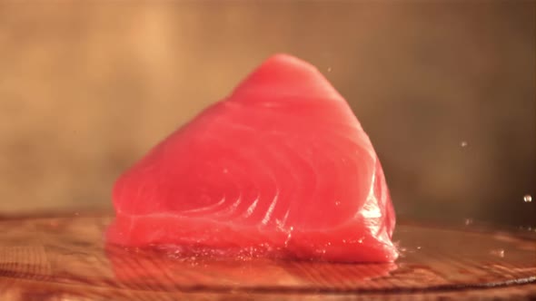 Super Slow Motion Fresh Tuna Steak Falls on a Cutting Board with Splashes of Water