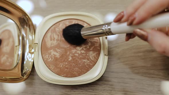 Makeup brush in a container with beige face shadows powder