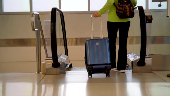 Woman rolls carry on luggage into the frame and gets on escalator and goes down.