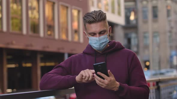 Portrait of Young Man in Medical Mask Is Texting Message Then Points To the Camera Smartphone with