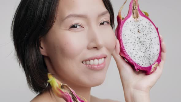 Mature Korean Lady Holding Dragon Fruit Near Face Gray Background