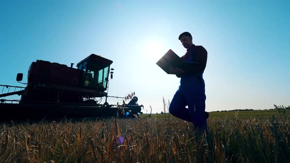 Agriscientist with a Laptop Is Near the Combine Machine