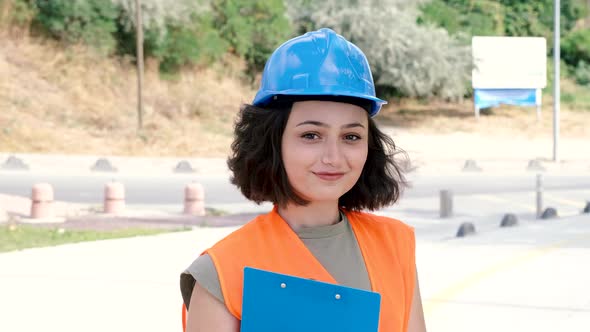 Portrait of a lovely cheerful young woman engineer or worker in a uniform and protective hardhat