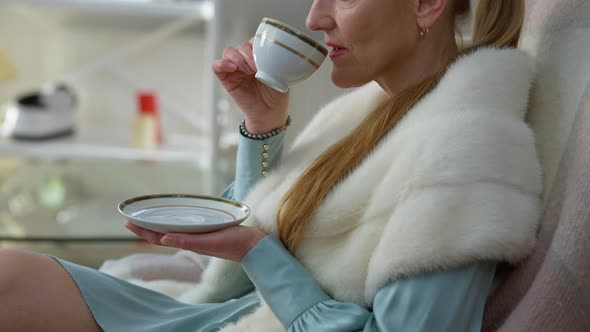 Unrecognizable Wealthy Caucasian Lady Drinking Tea Sitting at Home Indoors