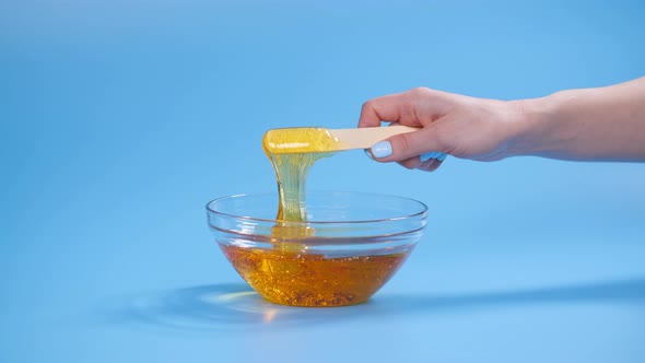 Beauty and Body Care Concept. Liquid Yellow Sugar Paste or Wax for Depilation on a Blue Background