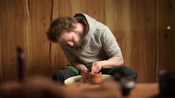 a bearded potter creates a clay pot in his workshop