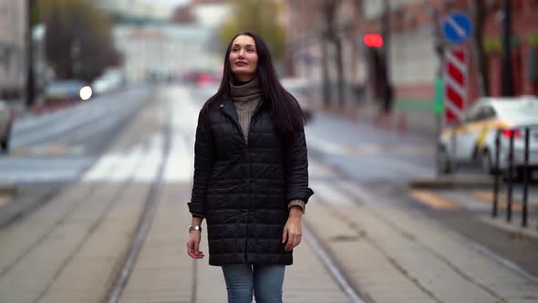 A Middle-aged Dark-haired Woman in a Black Jacket Walks on a City Street on an Autumn Day, Smiles