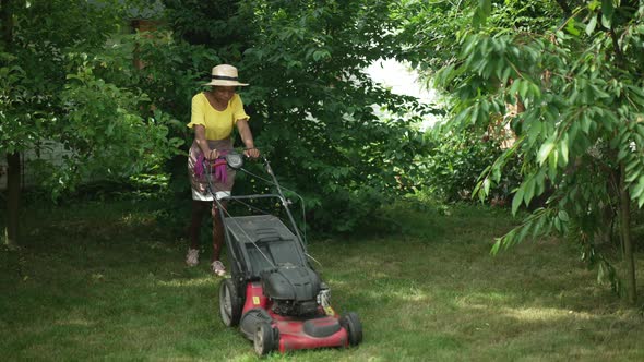 Wide Shot African American Young Woman Walking with Lawn Mower on Sunny Backyard Outdoors