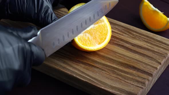 Man Slicing Raw Orange with Kitchen Knife on Wooden Cutting Board