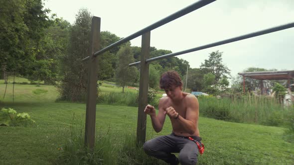 Young fit topless man stretches wrists before exercising on parallel bars at home gym