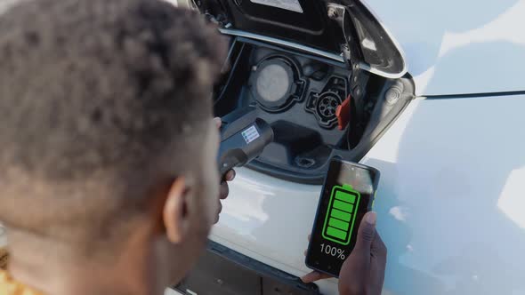 A Darkskinned Male Driver Connects an Electric Car to the Power System to Charge the Car Battery and