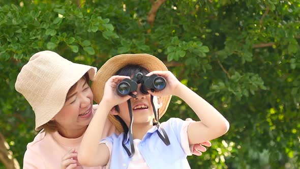 Asian Mother And Her Son Using Binocular And Pointing On Summer Day