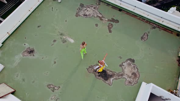 Drone Shot Of Models In Green And Yellow Dancing On City Rooftop