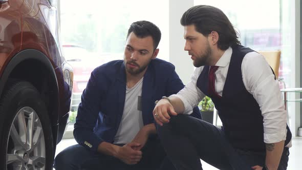 Male Friends Examining Wheels and Tires of a Car for Sale