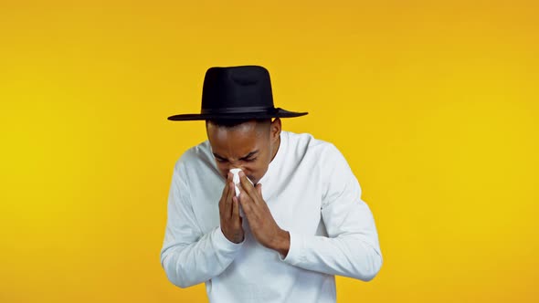 Young Hipster Man in Hat Sneezes Into Tissue. Isolated African Guy Is Sick, Has a Cold or Allergic