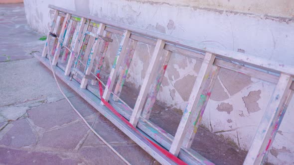 Long Stepladder Lies on Ground Near House Wall in Shadow