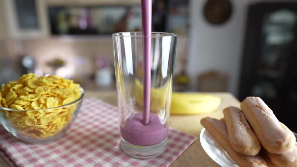 Pouring fresh berry smoothie into a transparent glass on a rotating table