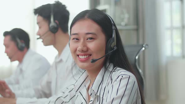 A Woman Of Three Asian Call Centre Agents Looking Up From Computer And Smiling To Camera