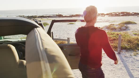 Caucasian man in sunglasses getting out of car and closing door on sunny day at the beach