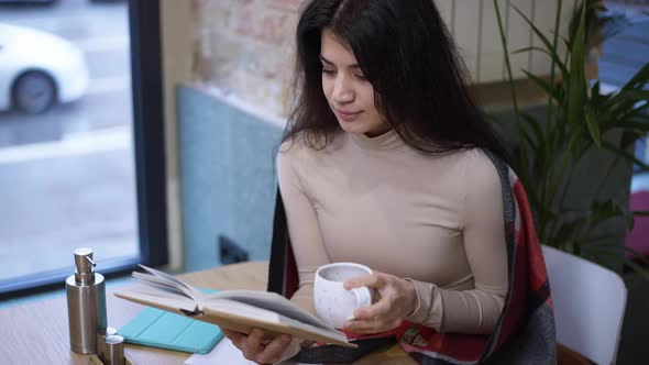 Gorgeous Smart Slim Beautiful Woman Reading Book Drinking Tea in Slow Motion Sitting at Table in