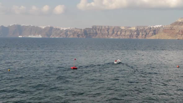 A small boat inside the majestic Santorini caldera. Cruise ships and cycladic villages can be seen i