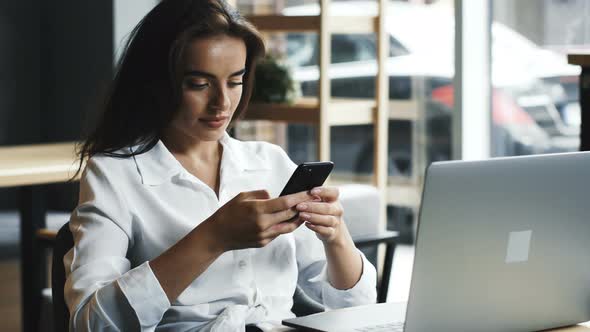 Handsome Businesswoman Sitting in Cafe with Laptop and Using Telephone with Smile