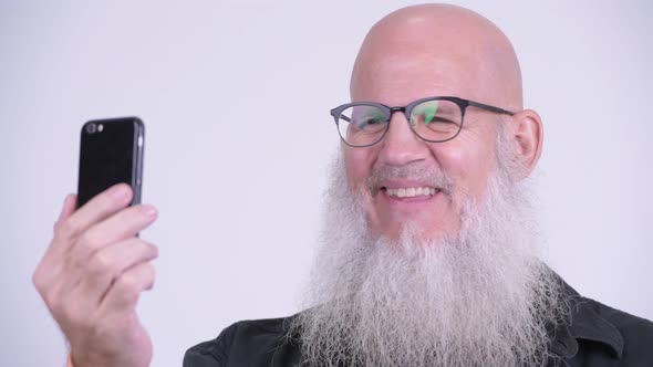 Face of Happy Mature Bald Bearded Man Smiling While Using Phone