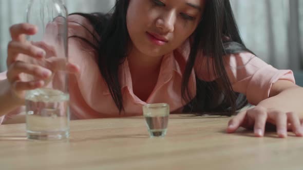 Drunk, Depressed Asian Woman With Smartphone On Table Pouring Vodka In A Shot Glass Before Drinking