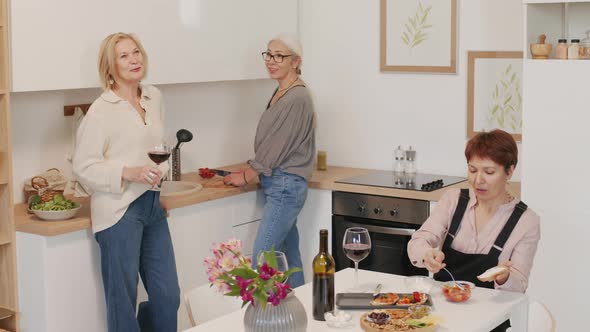 Three Mature Girlfriends Drinking Wine and Talking in Kitchen