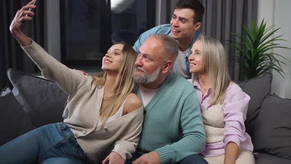 Cheerful Family Sitting on the Sofa in the Living Room a Girl Takes a Selfie with Relatives Children