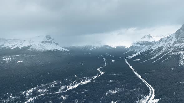 Bird's-eye drone footage of snowy mountains and dense dark winter forest in Alberta, Canada