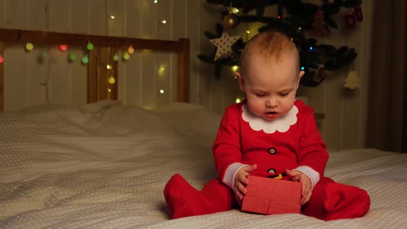 Christmas Baby in Red Santa Costume Playing on White Soft Bed