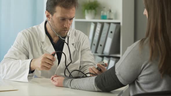 Middle-Aged Doctor Checking Female Patient's Blood Pressure at Hospital, Clinic