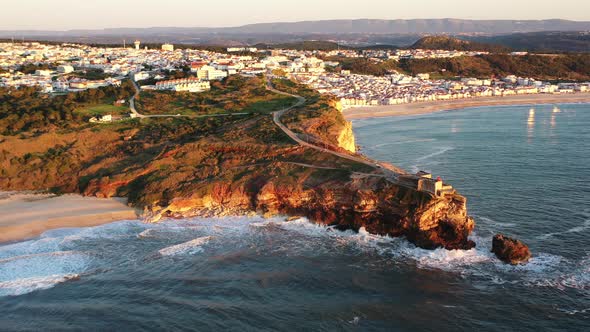 Nazare Portugal Lighthouse in Praia do Norte during sunset golden hour, Aerial dolly out