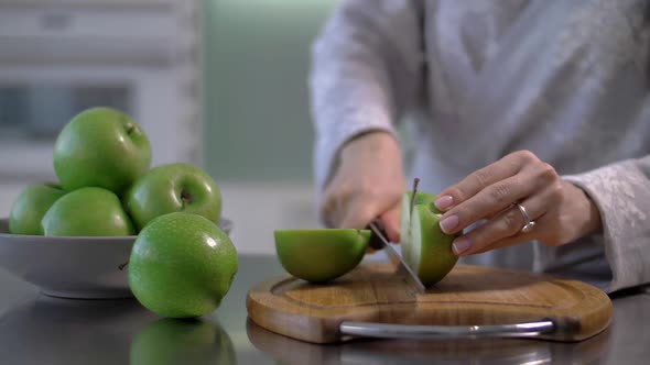 Young Woman Cuts a Juicy Apple on the Kitchen Table