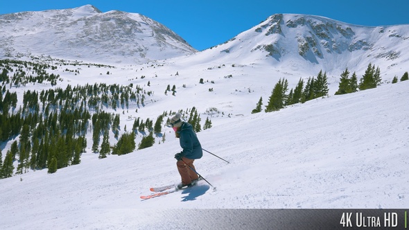4K Slow-Motion Tracking a Downhill Skier with Snow-Capped Rocky Mountain Range in the Background