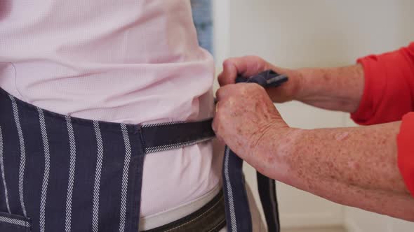 Midsection of senior couple in kitchen at home wife tying husband's apron before preparing meal