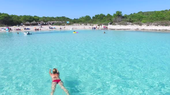 Attractive woman swimming among people in a white sandy bay