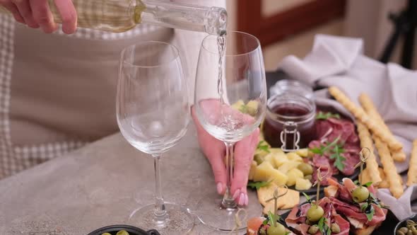 Woman Pouring Wine to a Glass From a Bottle at Domestic Kitchen with Meat and Cheese Plater on the