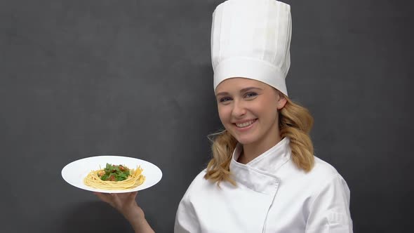 Happy Female Cook Holding Plate With Pasta and Smiling, Inviting to Restaurant