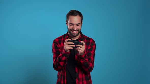 Man Playing Game on Smartphone on Blue Studio Wall. Using Modern Technology