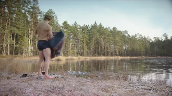 A fit muscular ice bather res his poncho and prepares to enter the frozen lake