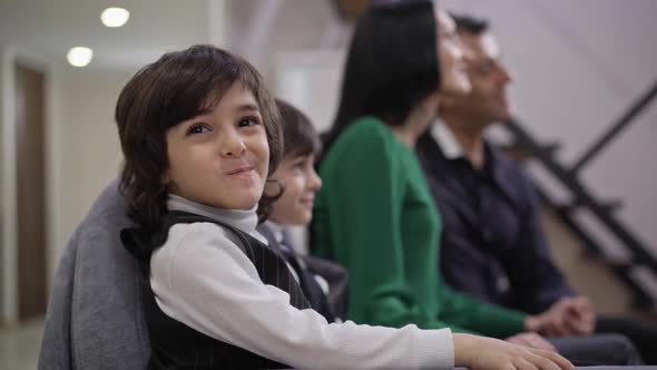 Happy Cute Boy Looking at Camera Smiling with Positive Family Resting at Background Watching TV