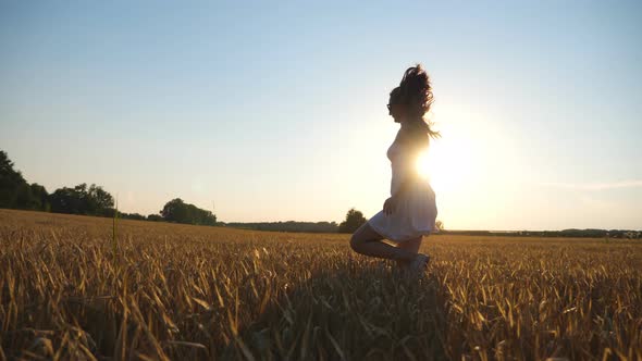 Unrecognizable Woman in White Dress Running Through Field with Yellow Wheat at Sunset