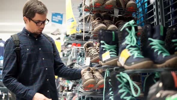 Man is Watching with Astonishment on a Pair of Male Shoes for Walking in a Shop