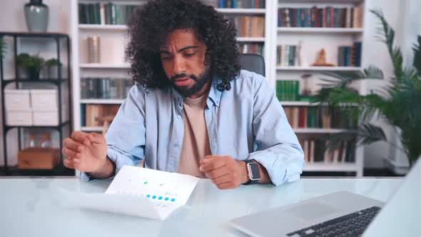 Puzzled Young Arabian Man Entrepreneur Examines Paper Financial Audit