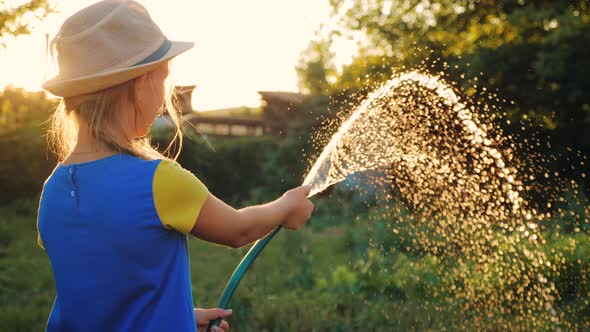 Funny Little Girl in Hat Playing with Garden Hose in Sunny Backyard. Adorable Little Girl Playing